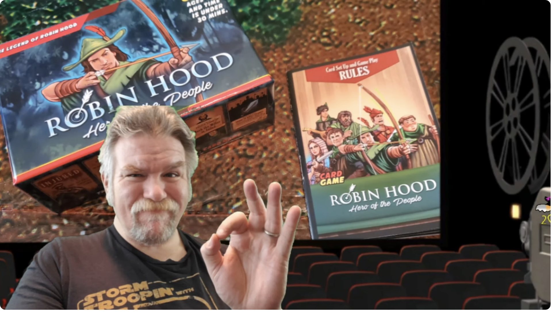 Video still: reviewer giving an OK sign in front of the Robin Hood box and rulebook